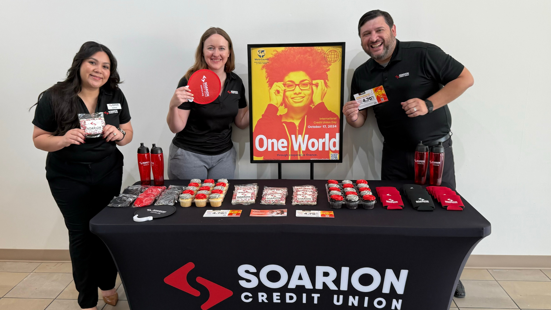 Group of soarion employees standing at a promo table for International Credit Union Day Group of soarion employees standing at a promo table for International Credit Union Day