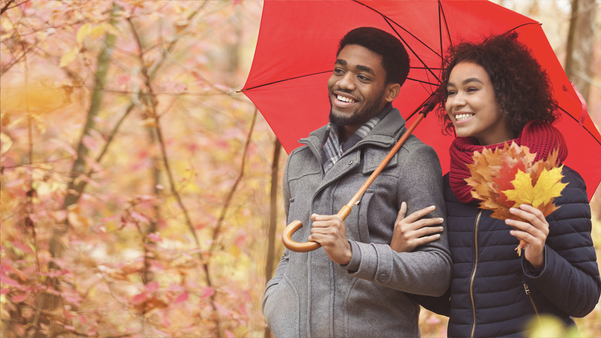 Couple walking through wooded area under red umbrella